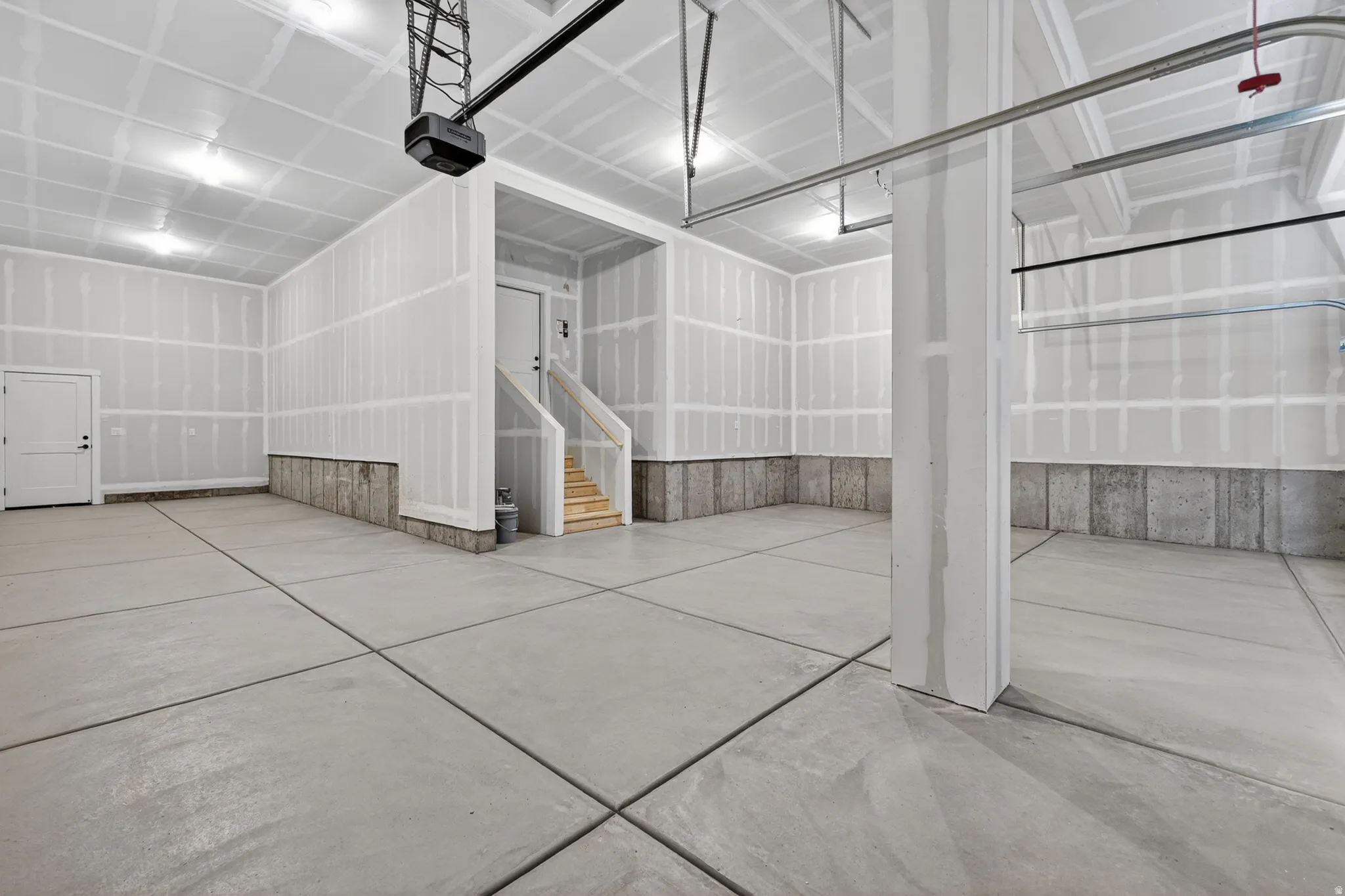 Spacious garage with a concrete floor, exposed drywall, overhead lighting, and an internal staircase