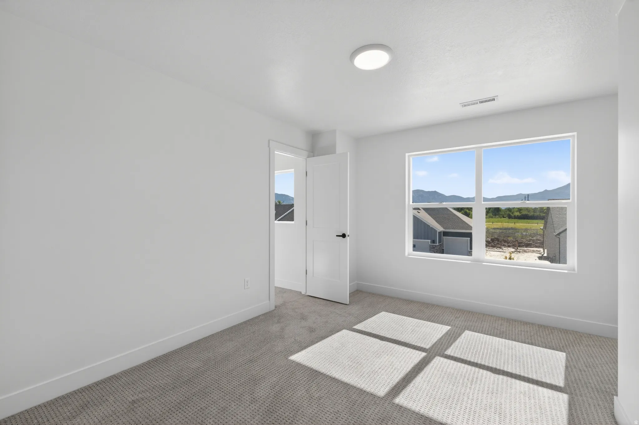 Bright interior space featuring a large window, light-colored walls, and gray patterned carpet