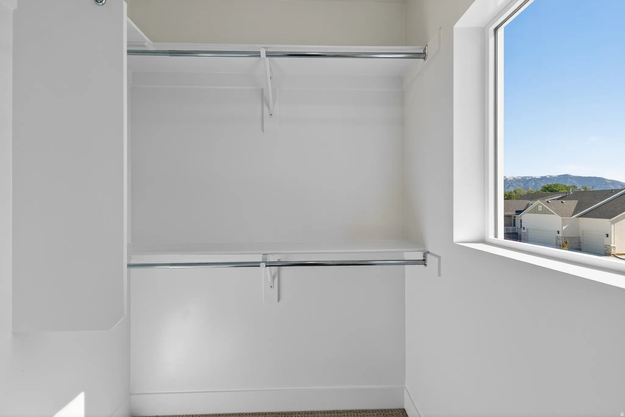 Walk-in closet featuring white walls, two integrated shelves, two chrome hanging rods, and a window with mountain scenery
