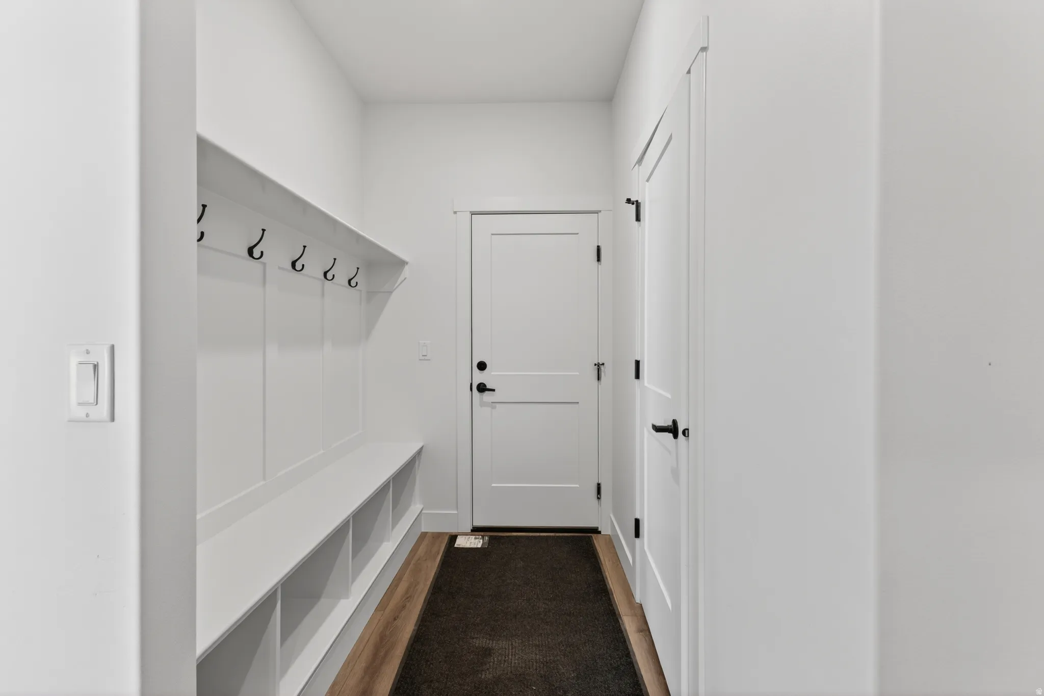 Entryway featuring a built-in bench, integrated cubbies, wall-mounted hooks, wood-finish flooring, and a paneled door with matte black hardware