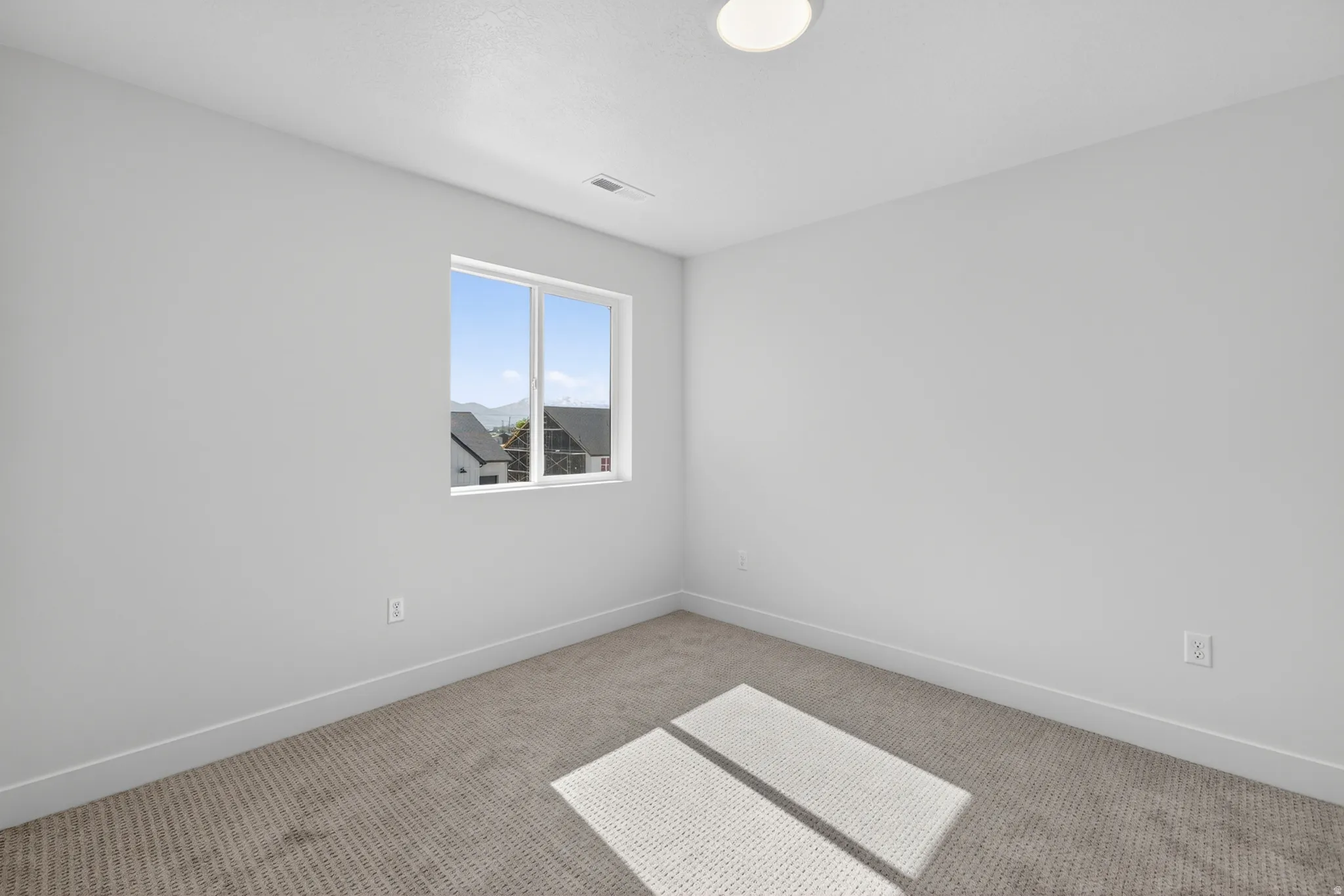 Carpeted room featuring a single window, white walls, and a flush-mount ceiling light