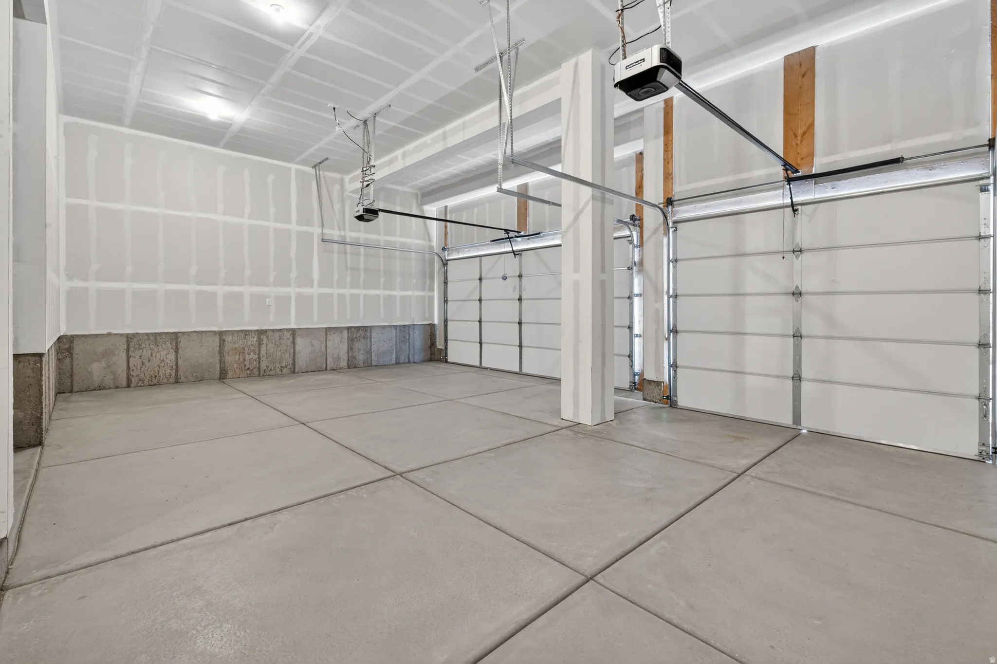 Spacious garage featuring a concrete floor, two white overhead doors, and exposed ceiling joists