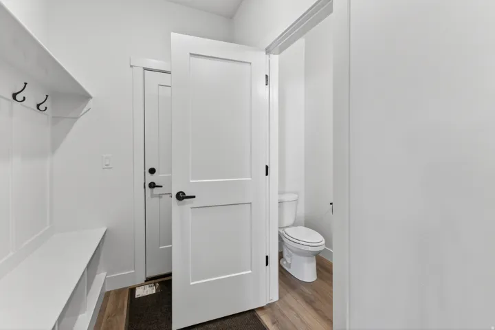 Entryway mudroom featuring a built-in bench with storage cubbies and coat hooks, wood-finish flooring, and a flat-panel interior door with matte black hardware