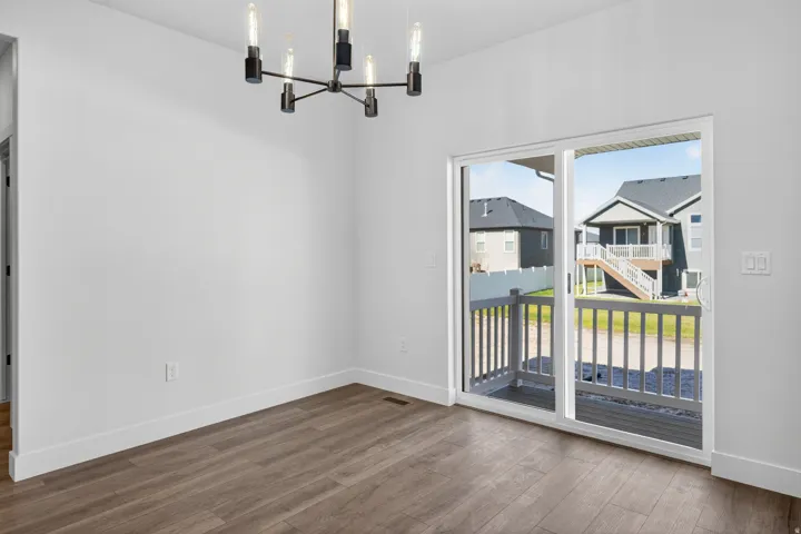 Spacious room featuring wood-finish flooring, a modern multi-bulb chandelier, white walls, and a sliding glass door providing access to a deck with white railings