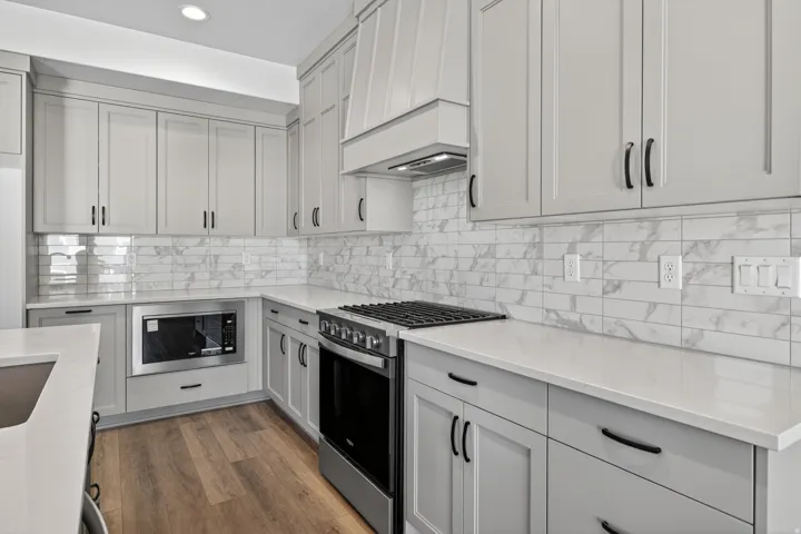 Modern kitchen featuring light gray shaker-style cabinetry, white countertops, and wood-finish flooring
