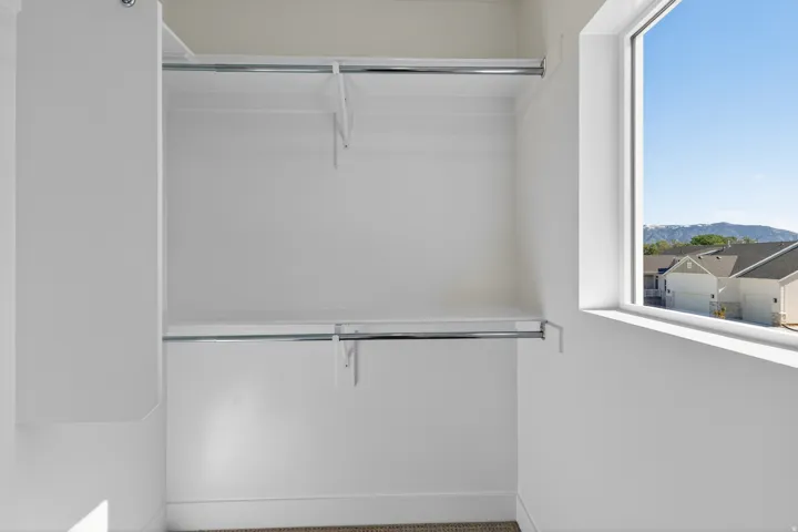 Walk-in closet featuring white walls, two integrated shelves, two chrome hanging rods, and a window with mountain scenery
