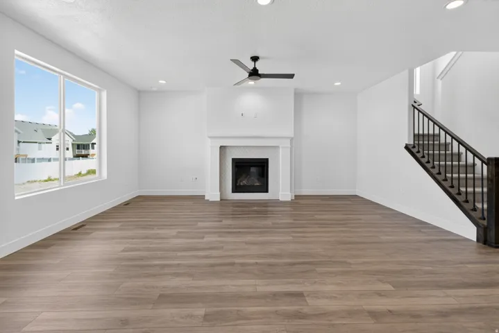 Spacious room featuring wood-finish flooring, a contemporary fireplace with a white mantel and tile surround, and a modern black ceiling fan
