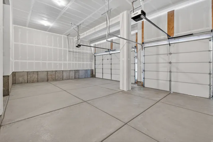 Spacious garage featuring a concrete floor, two white overhead doors, and exposed ceiling joists