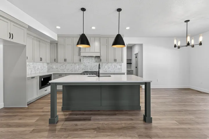 Open-concept kitchen featuring an oversized island with a light-toned countertop, gray cabinetry, a full height marble-look tile backsplash, wood-finish flooring, and black pendant lighting