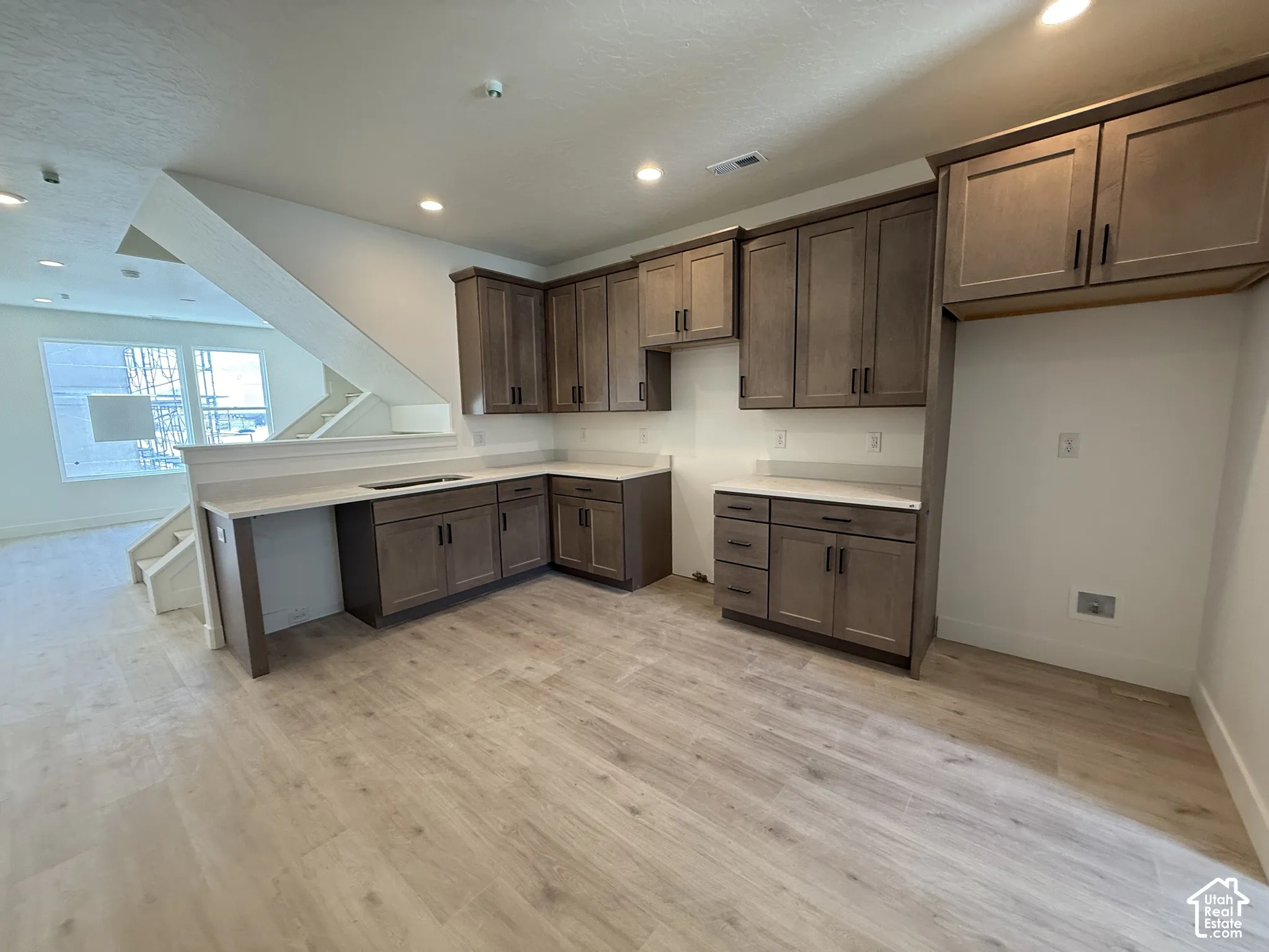 Contemporary kitchen featuring wood-finish flooring, light-toned countertops, and ample cabinetry with dark hardware