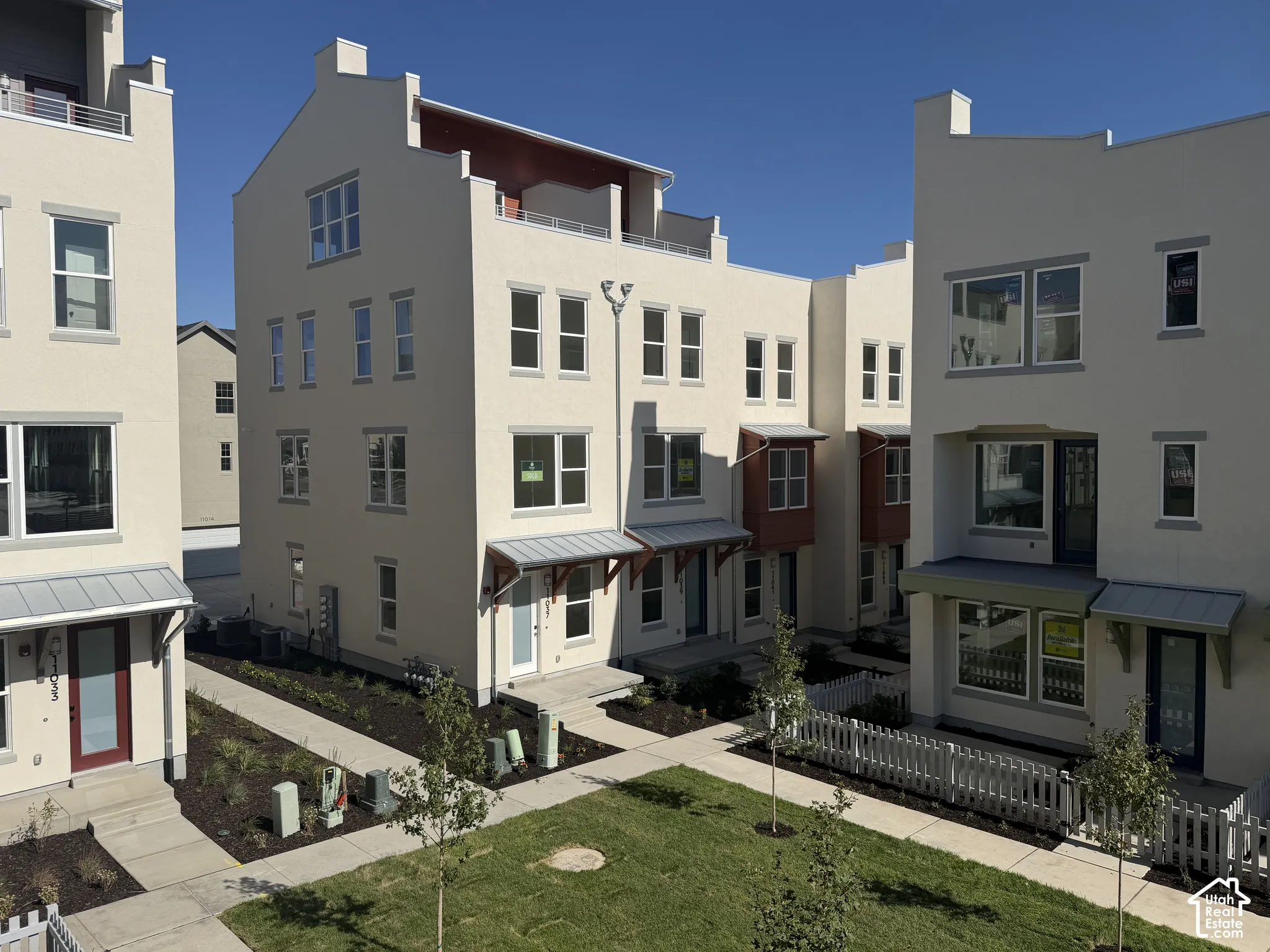Contemporary stucco townhomes featuring multiple windows, metal awnings, and a shared green space