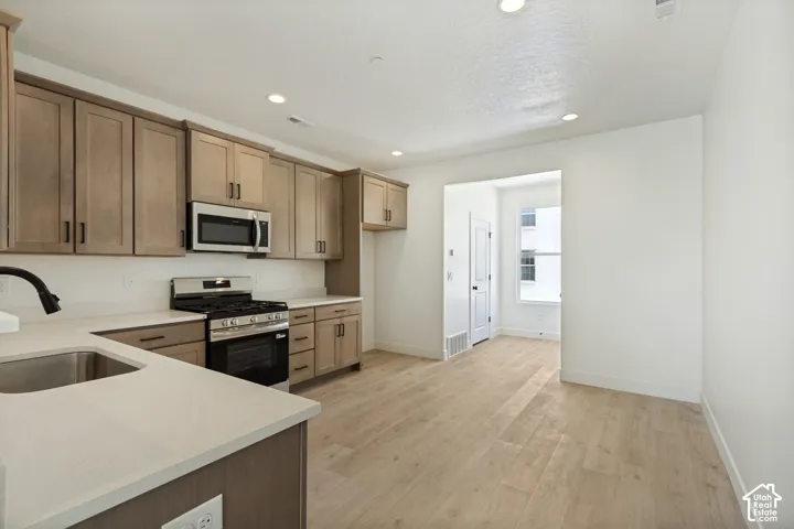 Kitchen featuring wood-finish cabinetry, stainless steel appliances, light-toned countertops, and wood-finish flooring