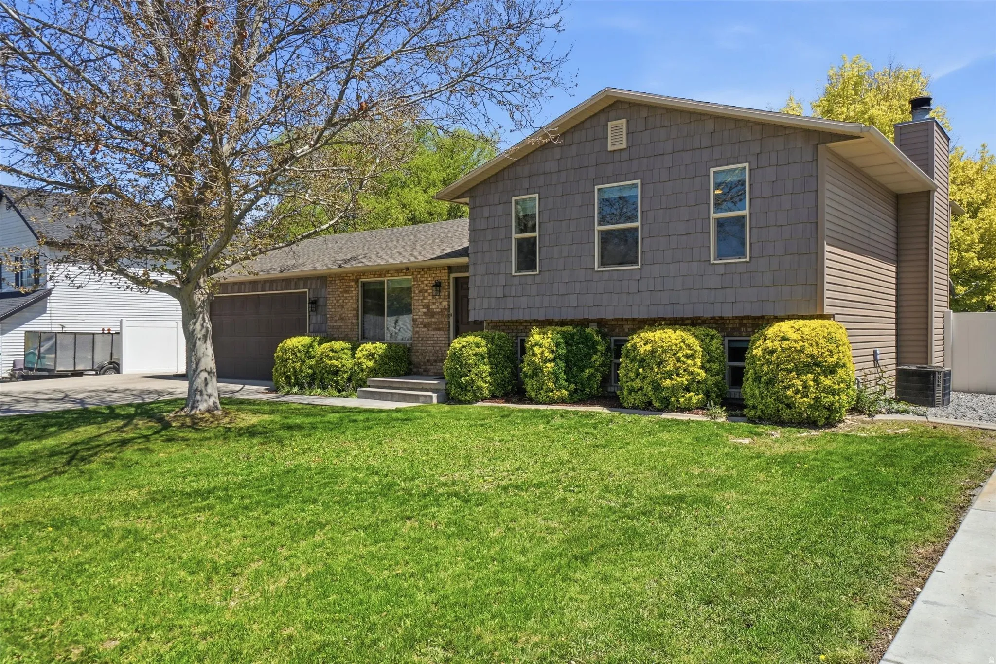 Tri-level home with an attached garage, concrete driveway, a chimney, and brick siding