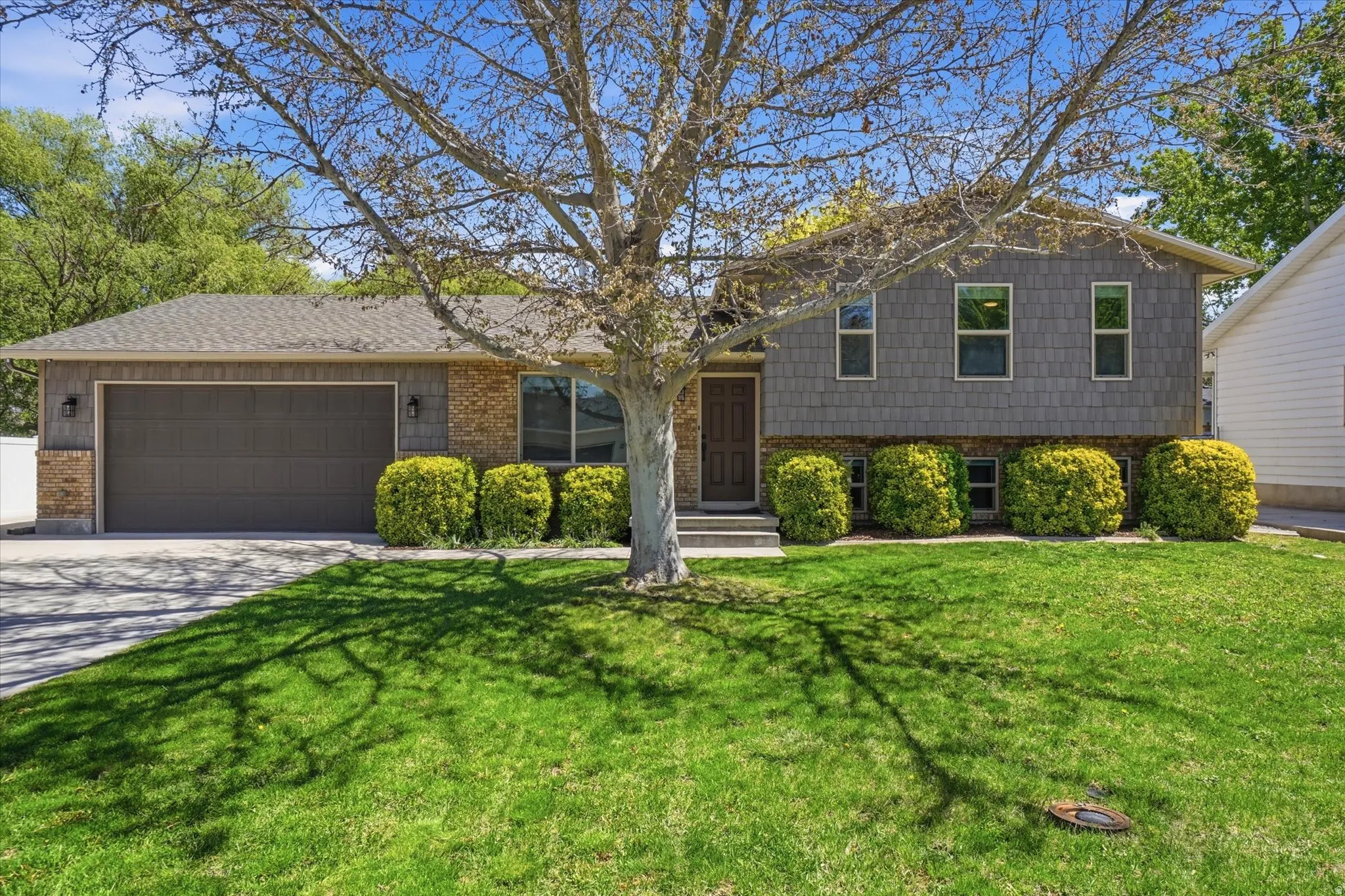 Split level home with brick siding, a garage, concrete driveway, and a front lawn