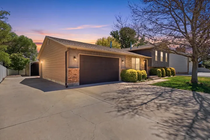 Split level home with concrete driveway, an attached garage, roof with shingles, and brick siding