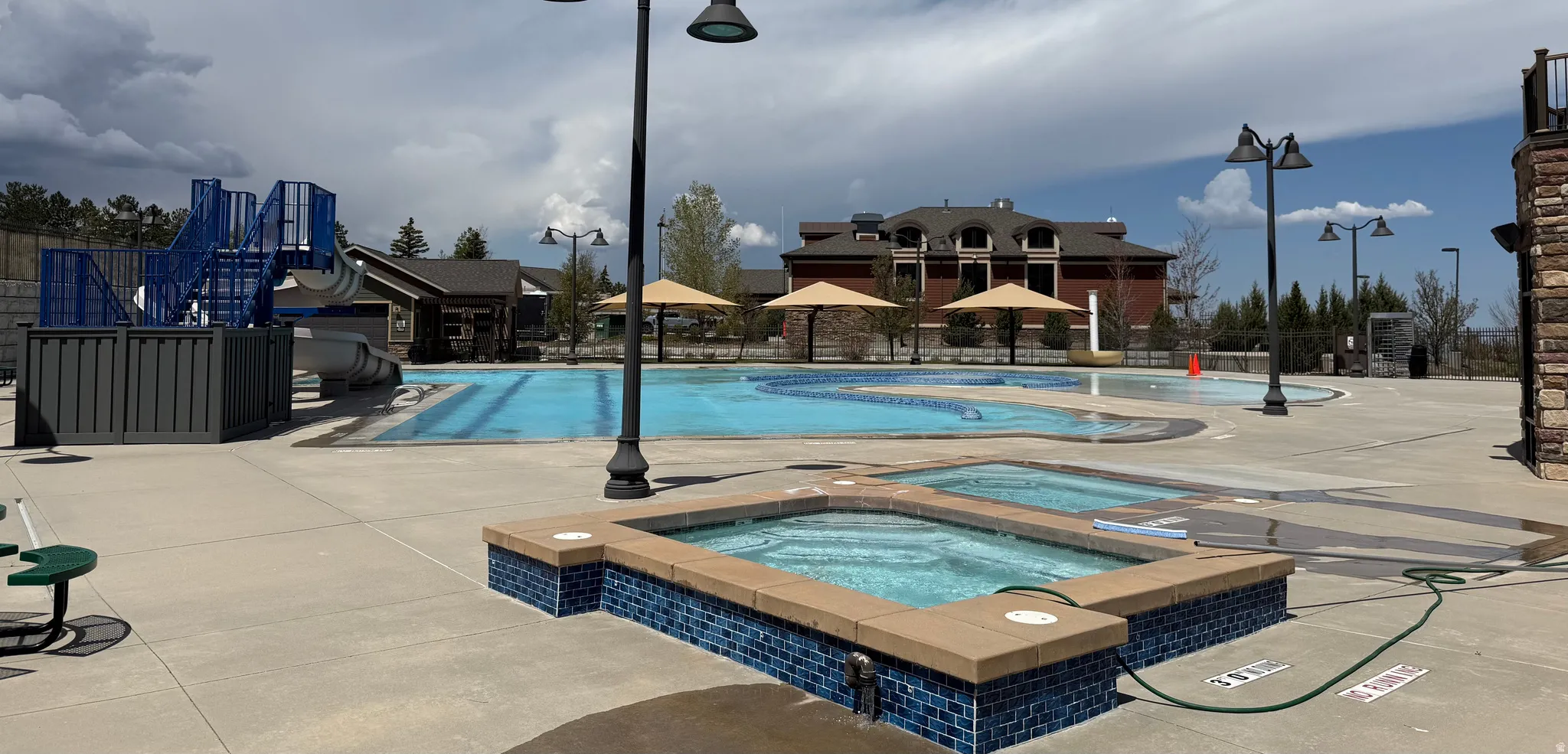 Spacious outdoor pool area featuring two in-ground hot tubs with blue mosaic tile surrounds, a large swimming pool, and an adjacent play structure with a slide