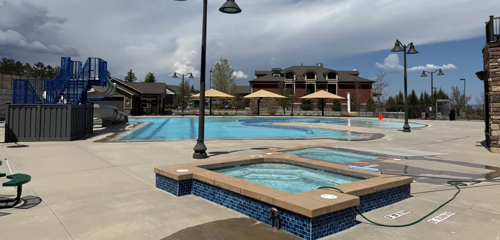 Spacious outdoor pool area featuring two in-ground hot tubs with blue mosaic tile surrounds, a large swimming pool, and an adjacent play structure with a slide