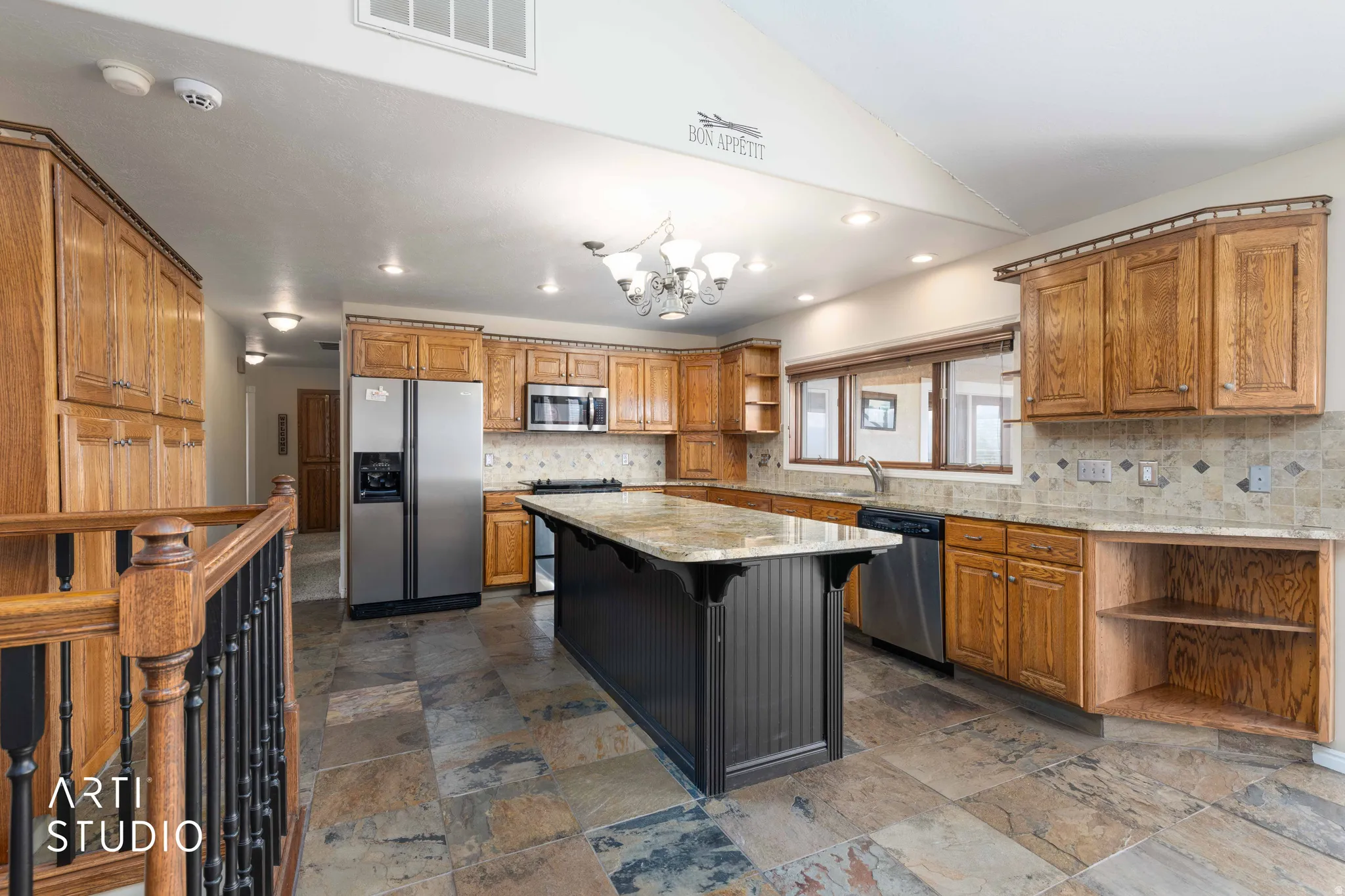 Kitchen with open shelves, wood finish cabinetry, a breakfast bar, stainless steel appliances, and light stone counters