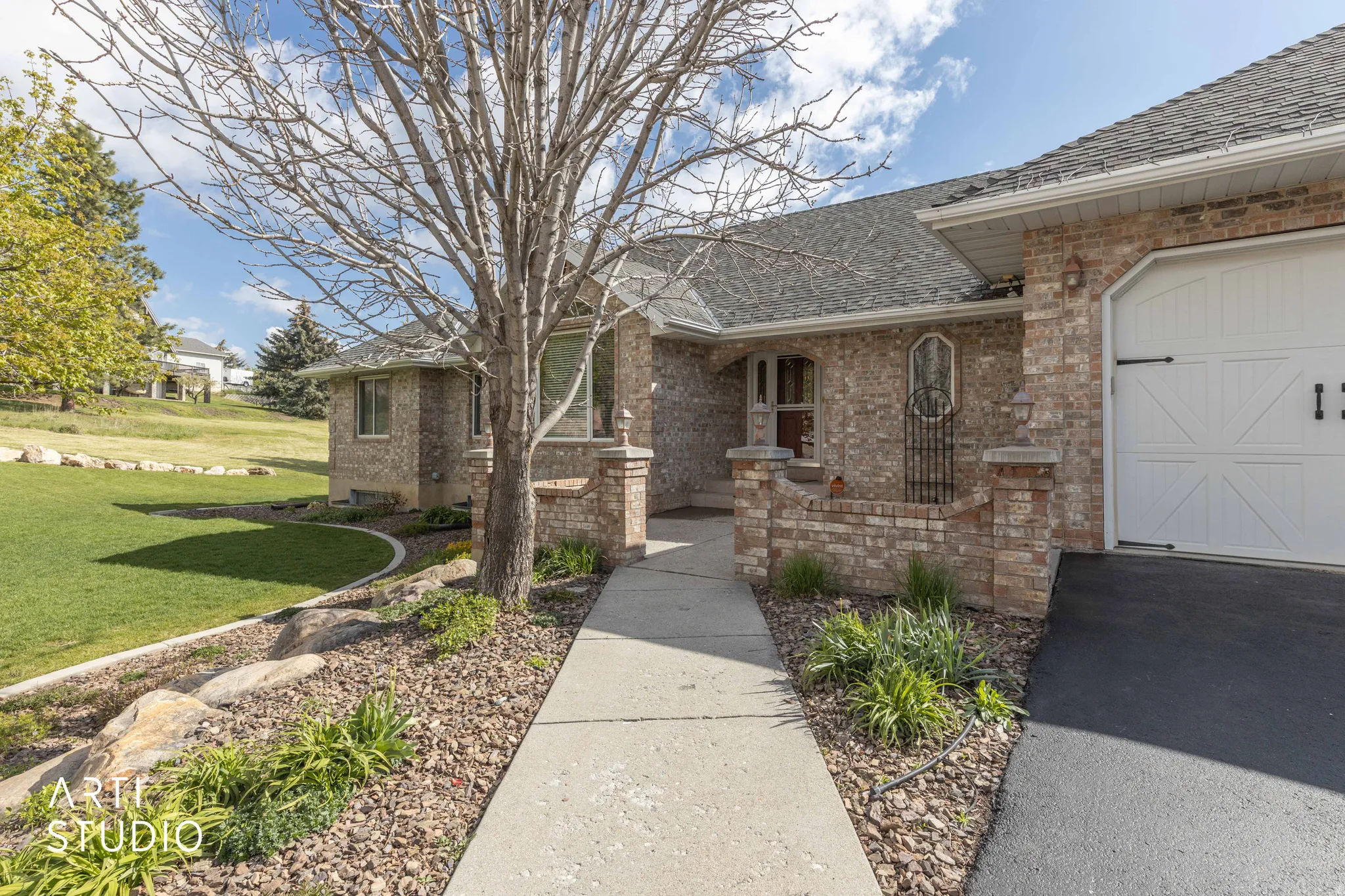 Entrance to property with a shingled roof, a yard, brick siding, a garage, and asphalt driveway
