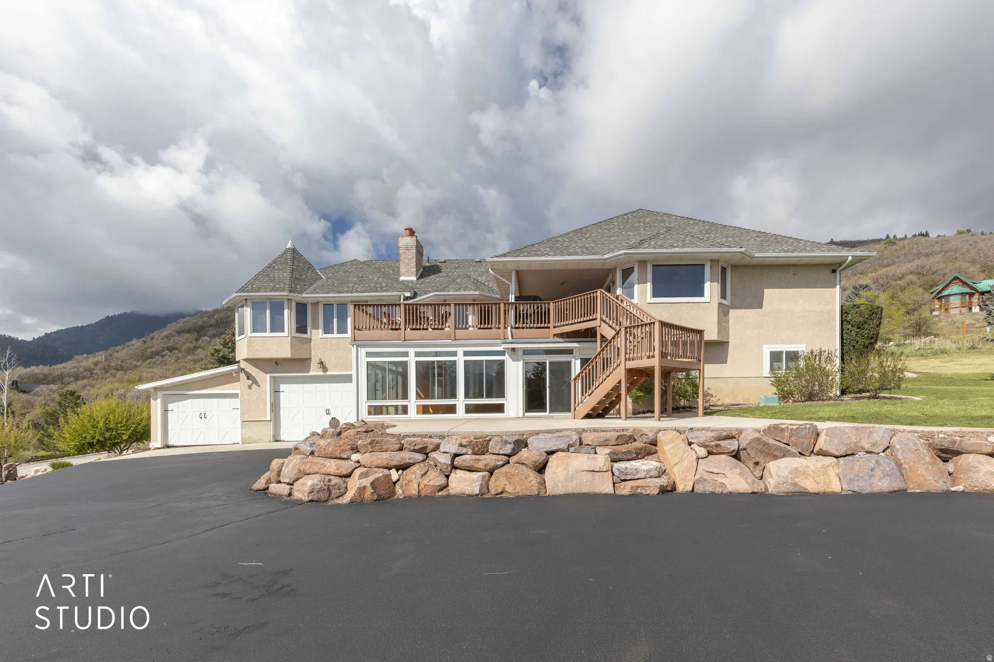 View of front of home featuring a deck with mountain view, a chimney, stucco siding, an attached garage, and asphalt driveway
