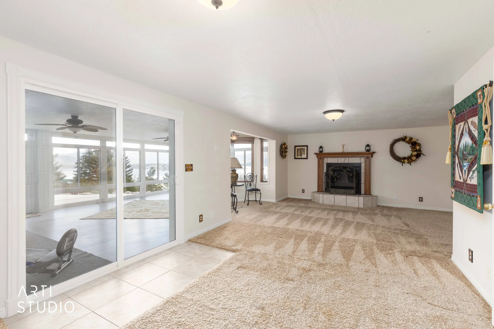 Unfurnished living room with a tile fireplace, light colored carpet, light tile patterned floors, and a ceiling fan