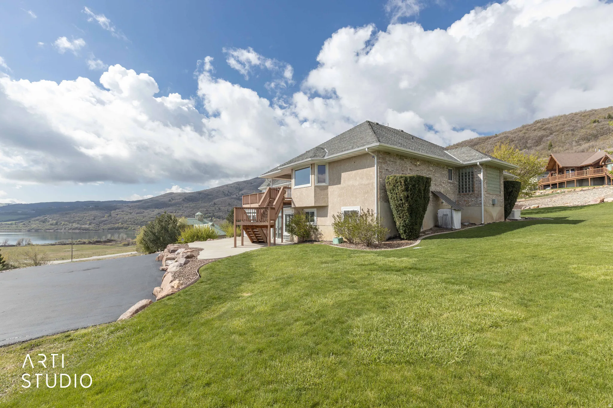 View of home's exterior featuring a deck with water view, a lawn, brick siding, and roof with shingles