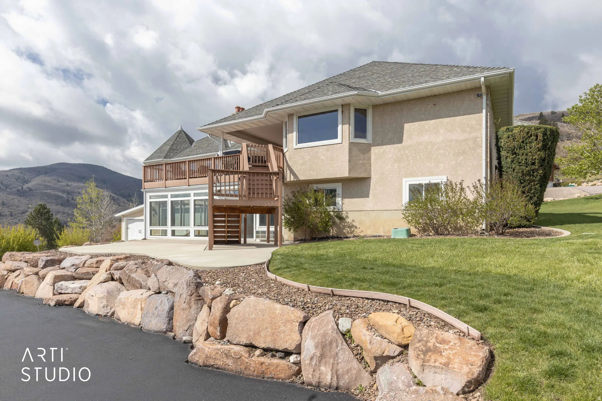 Back of property featuring stucco siding, a lawn, a shingled roof, a deck with mountain view, and a garage
