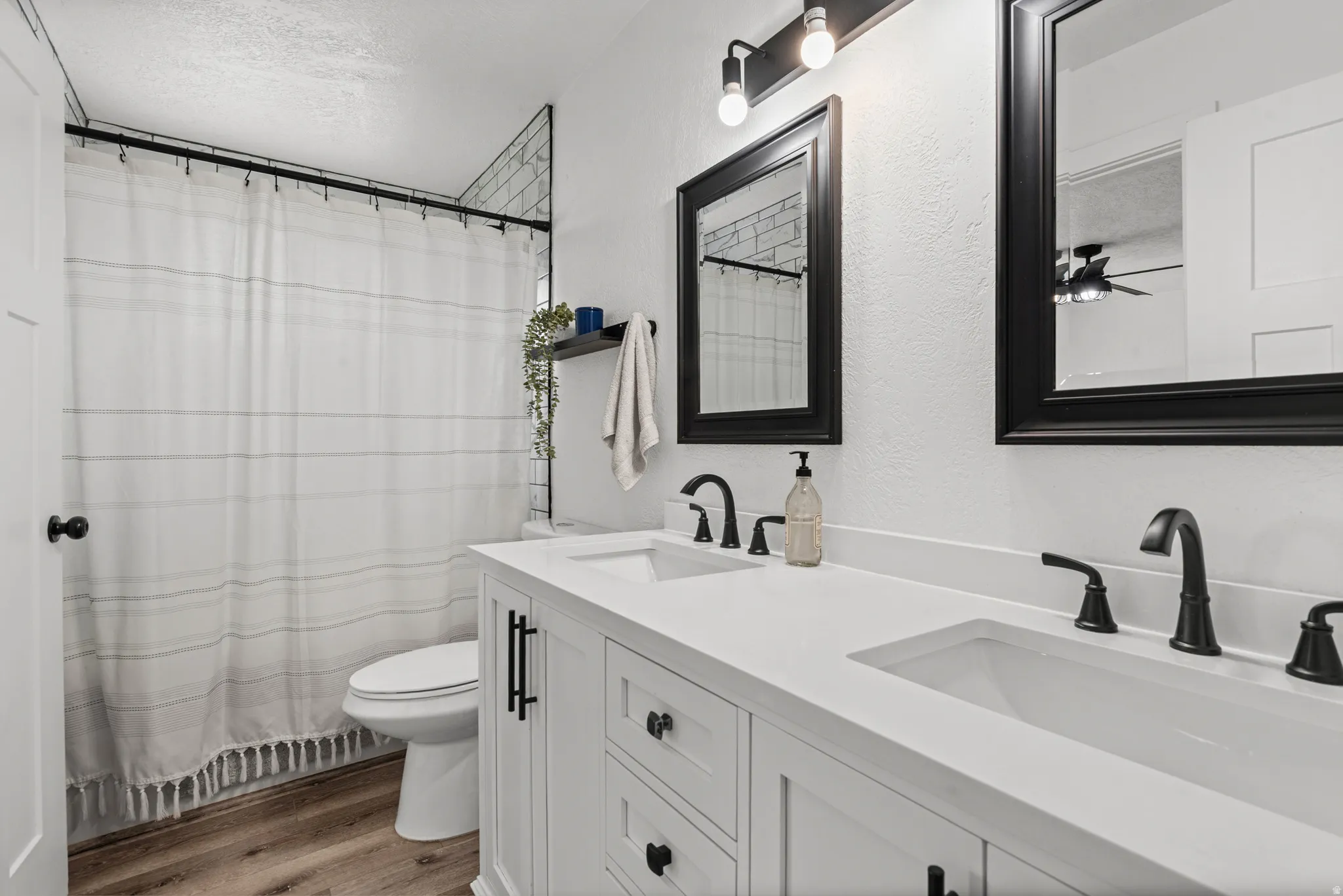Full bath with a shower with shower curtain, double vanity, light wood-type flooring, a textured ceiling, and a textured wall