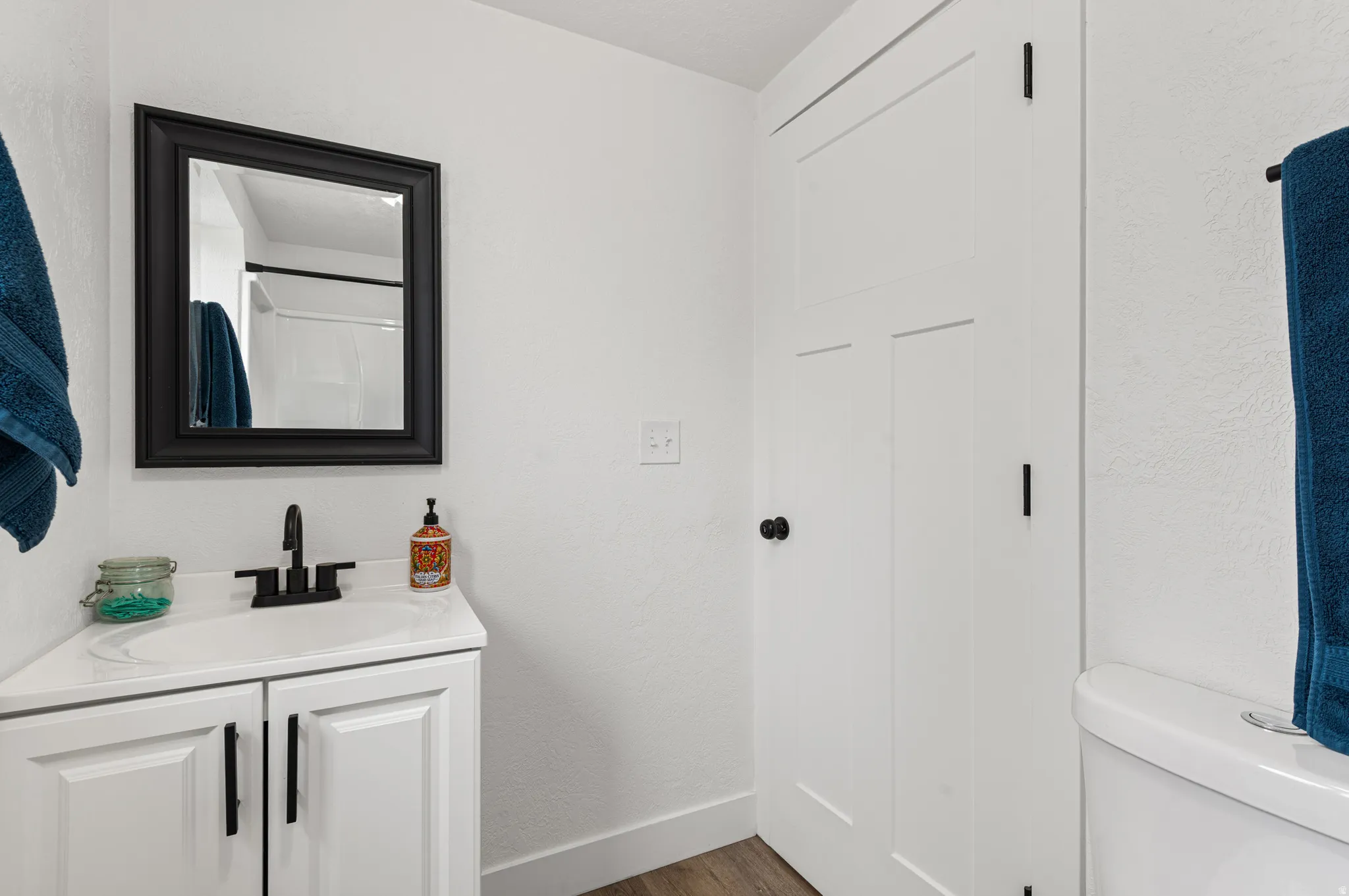 Bathroom with a textured wall, vanity, dark wood finished floors, and a shower with curtain