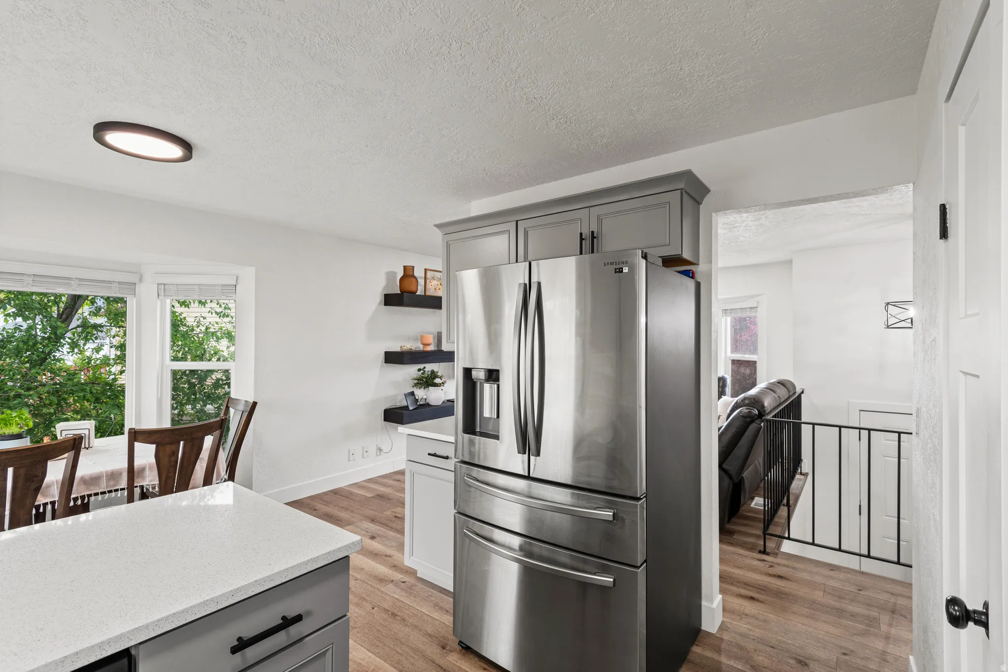 Kitchen featuring gray cabinetry, stainless steel refrigerator with ice dispenser, light wood-style floors, a textured ceiling, and light stone counters