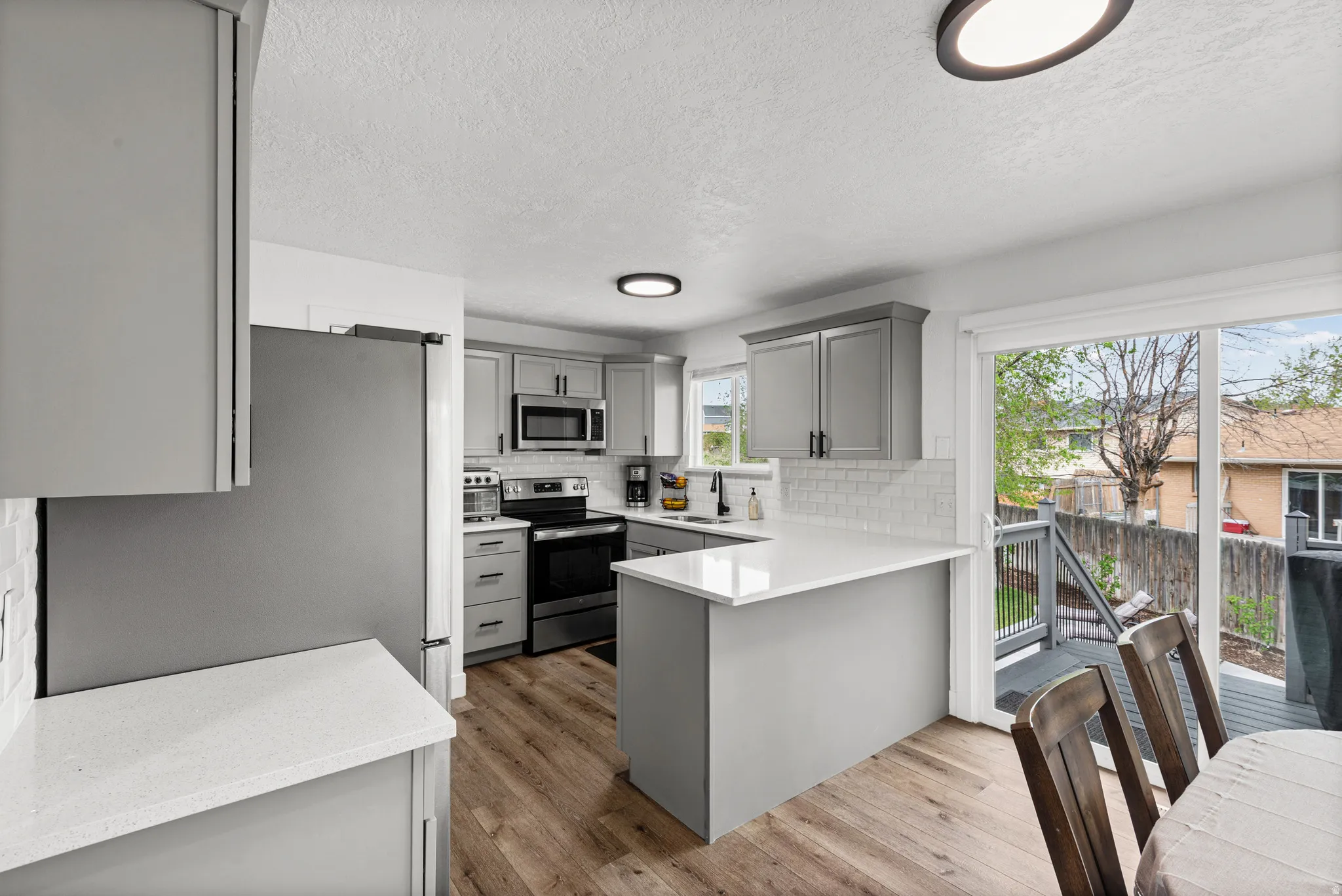 Kitchen with gray cabinetry, stainless steel appliances, light wood-style floors, a peninsula, and decorative backsplash