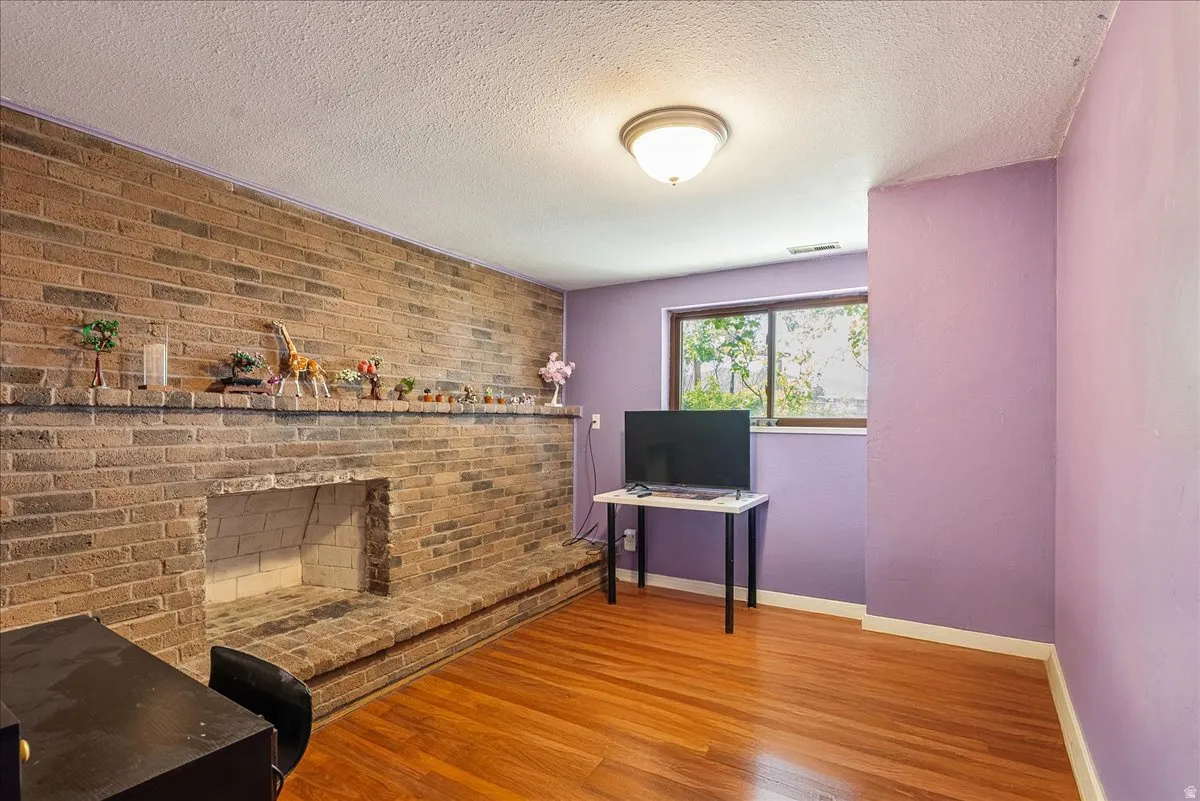 Home office with wood finished floors, a fireplace, a textured ceiling, and brick wall