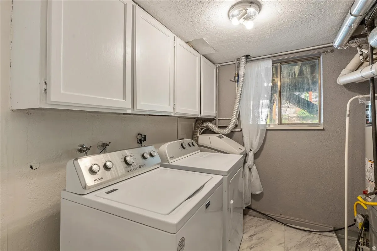 Laundry room featuring a textured wall, a textured ceiling, washer and clothes dryer, and cabinet space