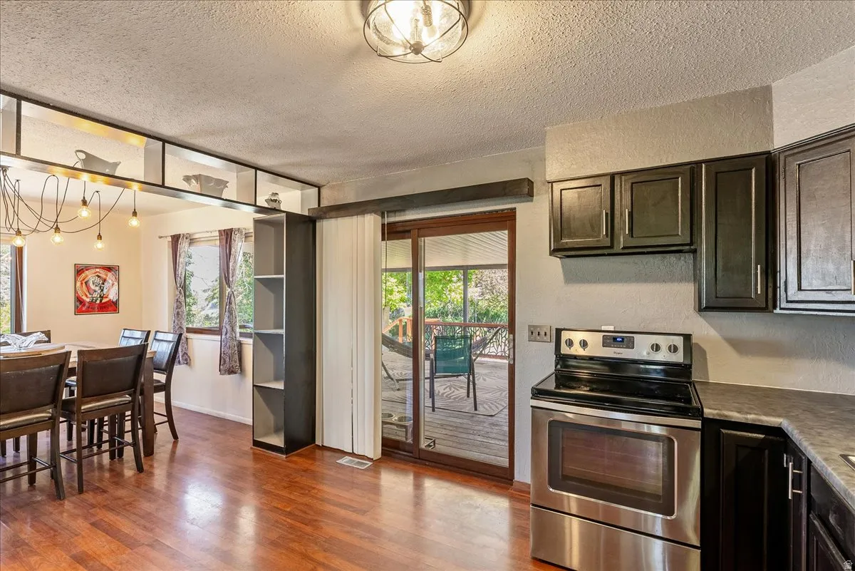 Kitchen with stainless steel range with electric stovetop, a textured ceiling, dark wood finish cabinetry, dark wood-type flooring, and healthy amount of natural light