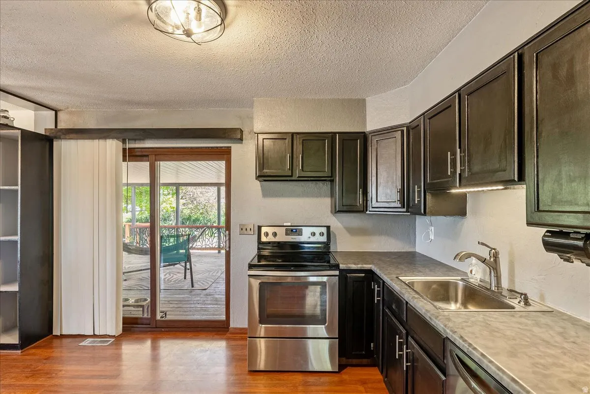 Kitchen with stainless steel appliances, a textured ceiling, dark wood finish cabinets, light wood-style floors, and light countertops