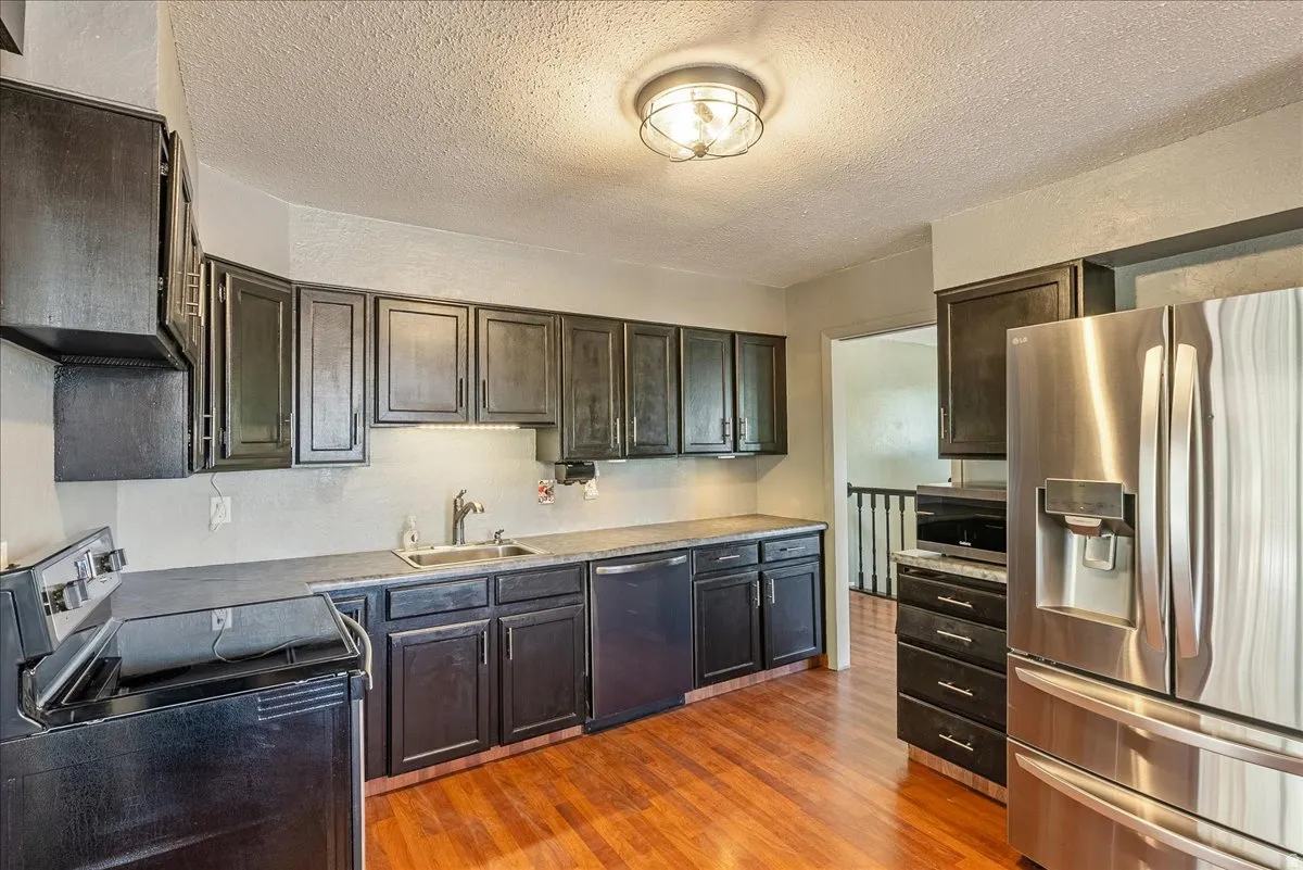 Kitchen featuring stainless steel appliances, dark wood finish cabinets, a textured ceiling, light wood finished floors, and light countertops