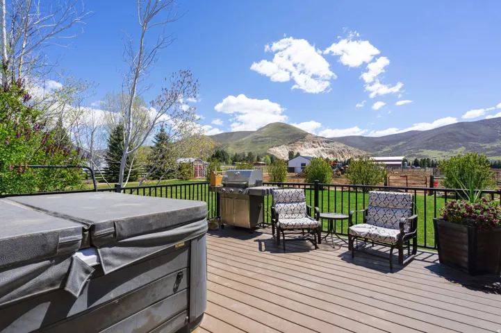 Deck with a hot tub, area for grilling, a mountain view, and a lawn