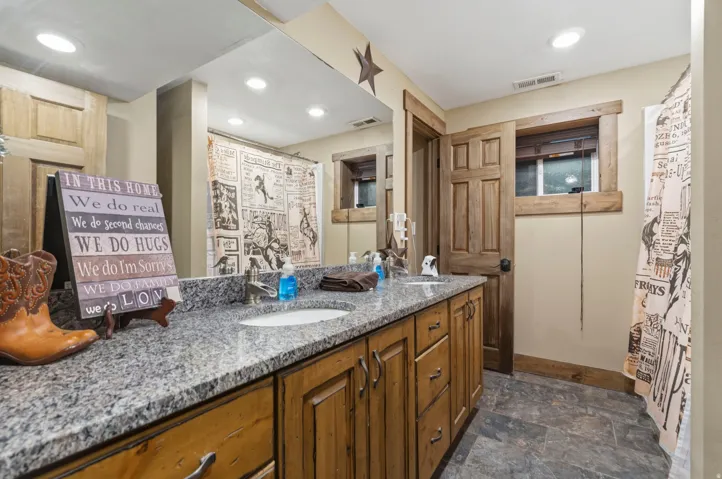 Full bathroom featuring double vanity, dark stone finish flooring, a shower with shower curtain, and recessed lighting
