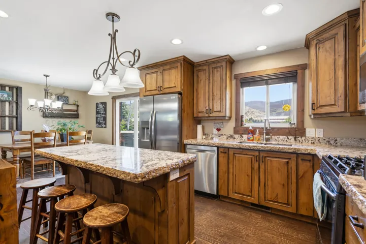 Kitchen with wood finish cabinetry, light stone counters, a center island, stainless steel appliances, and dark wood-type flooring