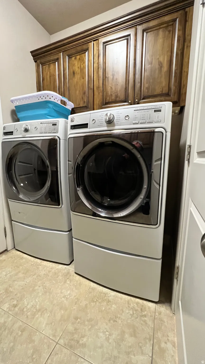 Laundry room with washing machine and clothes dryer, cabinet space, and light tile patterned floors