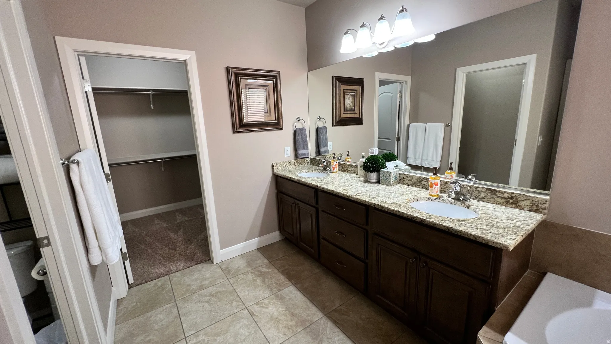 Bathroom with double vanity, light tile patterned floors, and a walk in closet