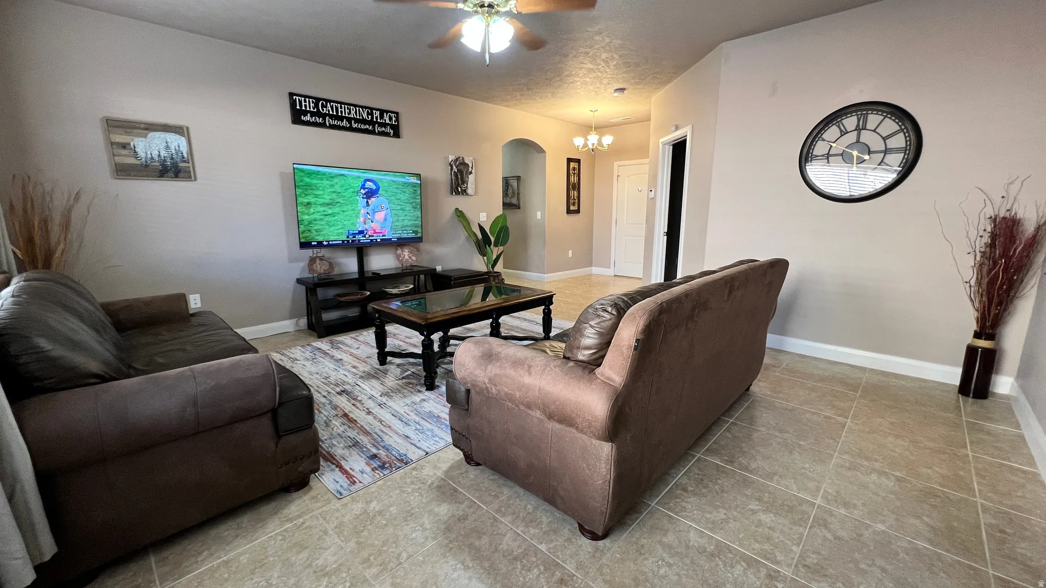 Living room with arched walkways, ceiling fan, light tile patterned floors, and a chandelier
