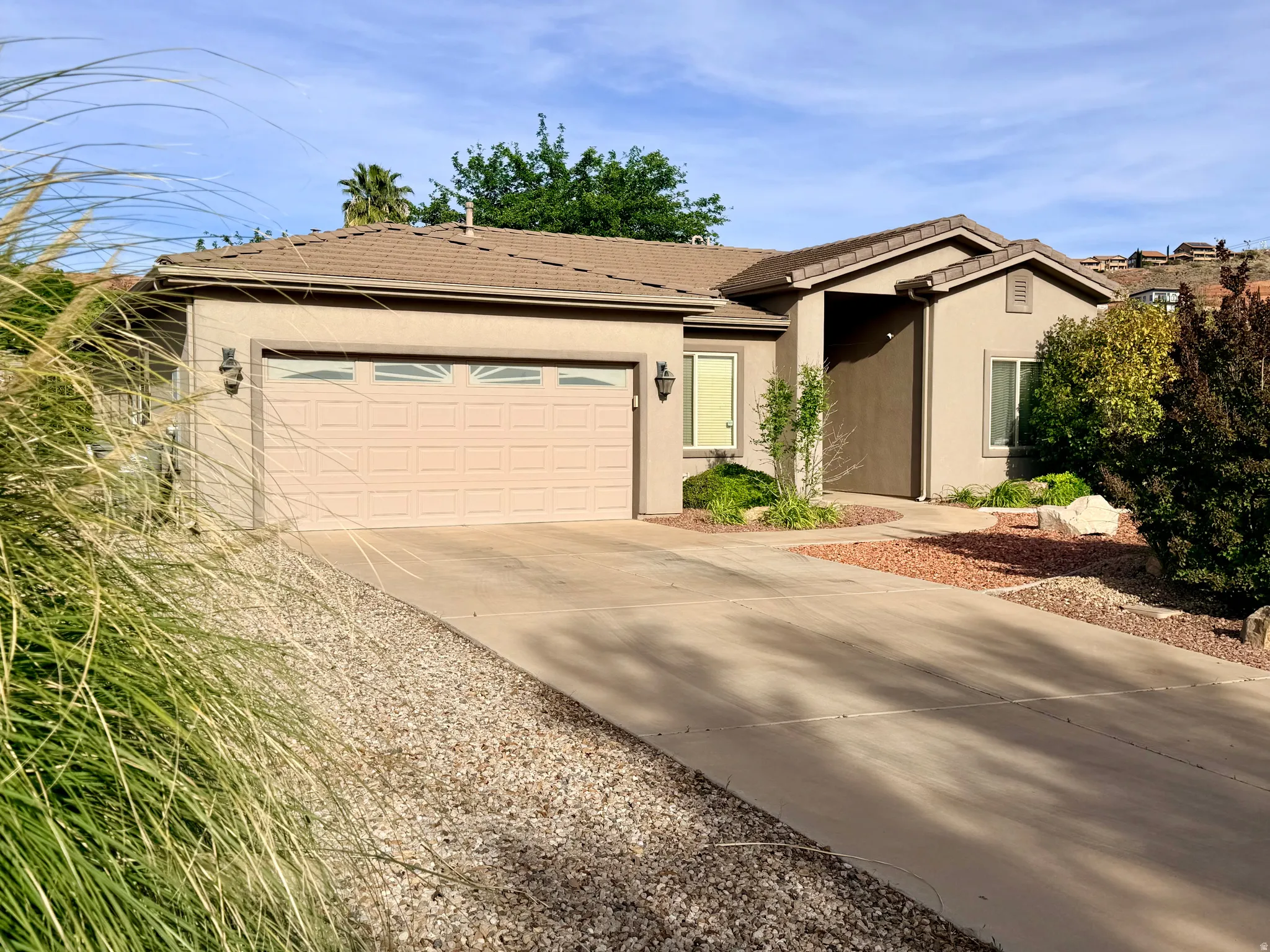 Single story home featuring a tiled roof, stucco siding, driveway, and a garage