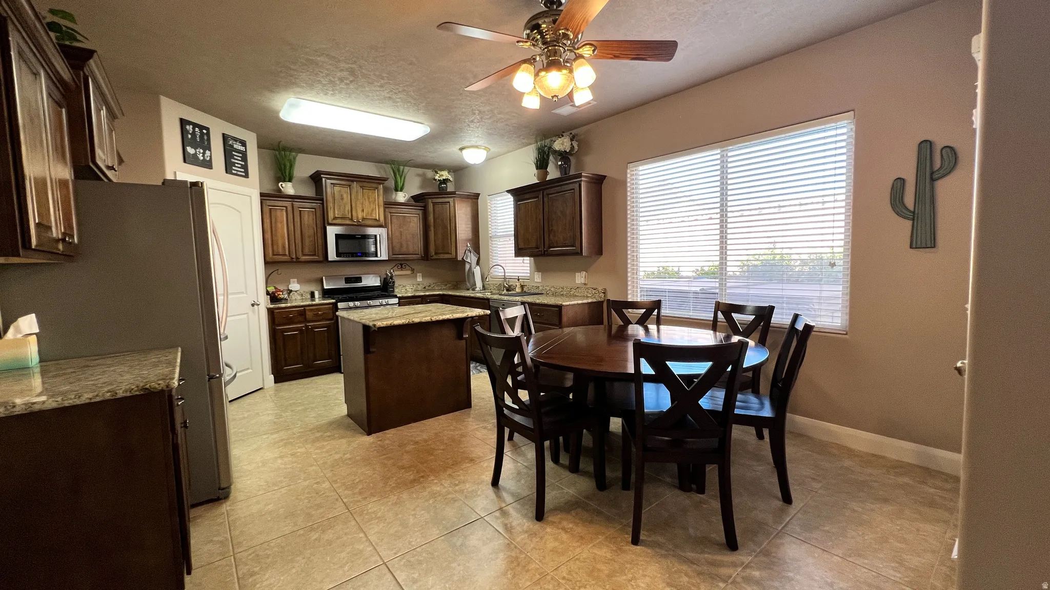 Kitchen with dark wood finish cabinets, ceiling fan, a center island, a textured ceiling, and stainless steel appliances