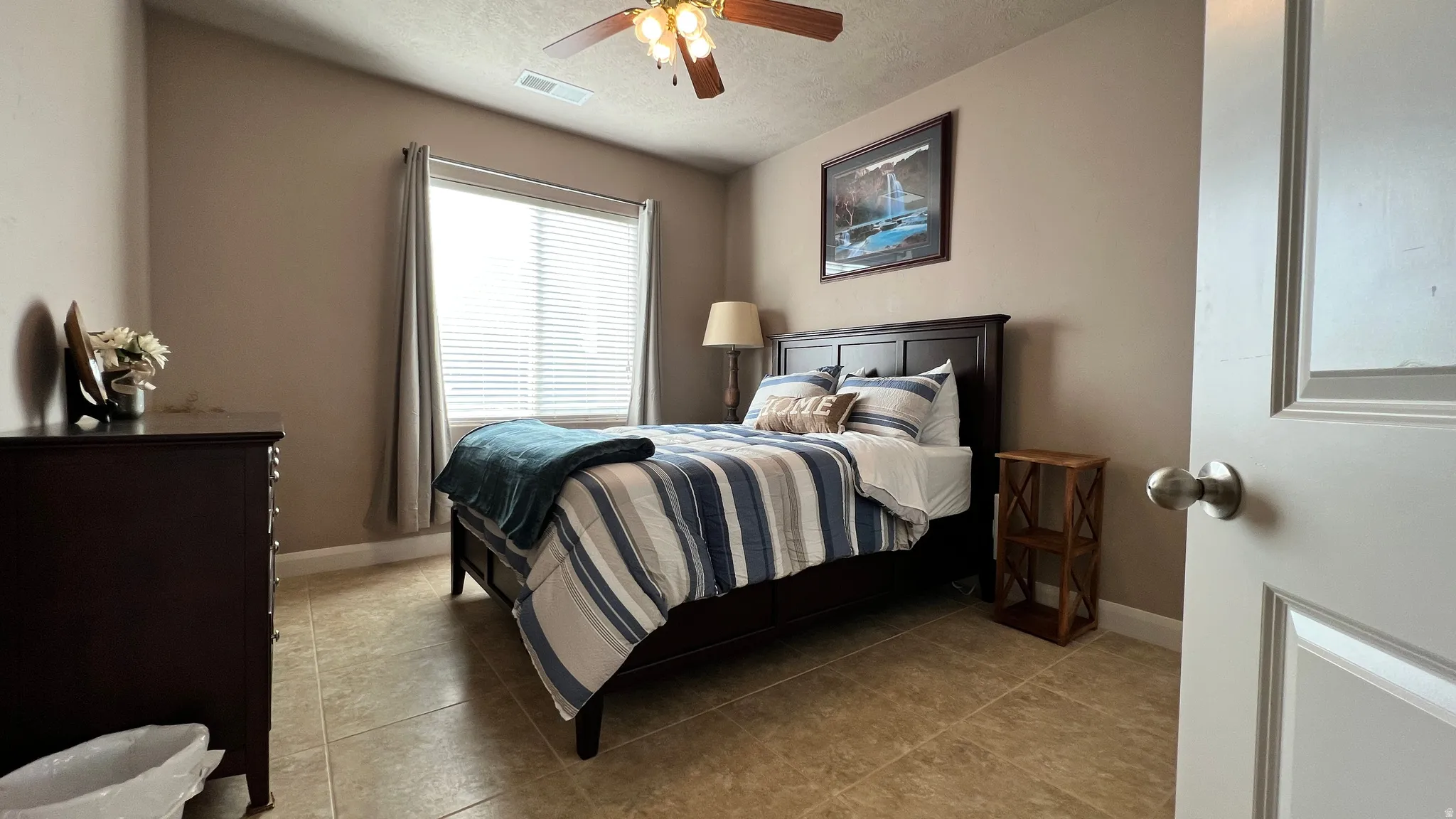 Bedroom featuring a ceiling fan, light tile patterned floors, and a textured ceiling