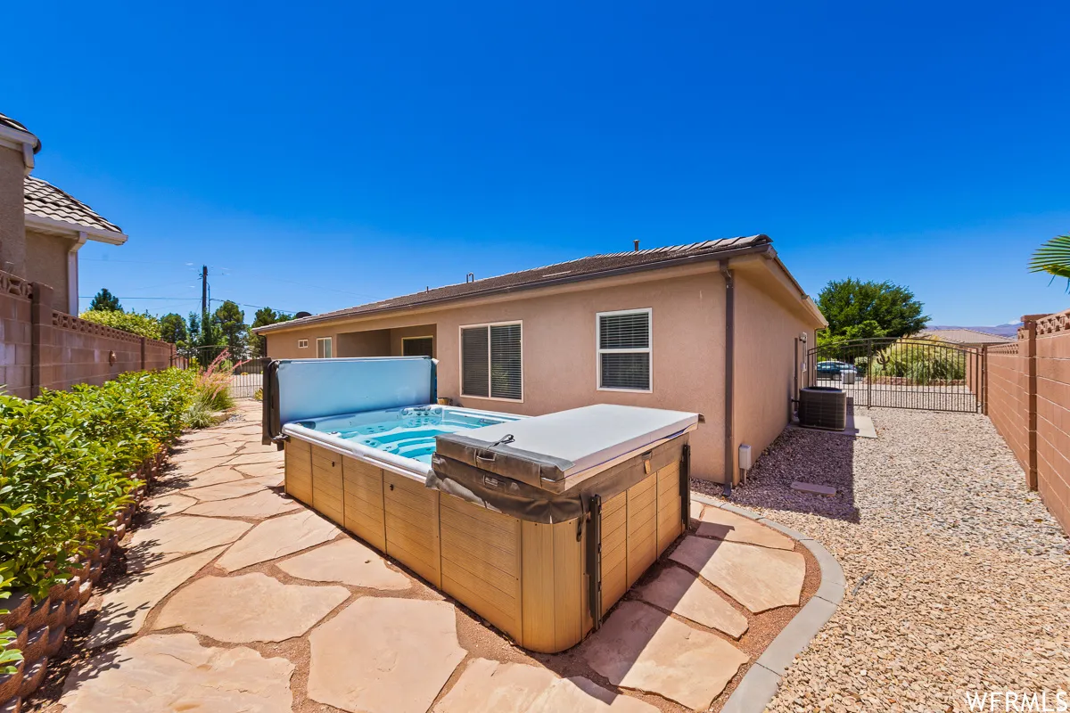 Rear view of house with a fenced backyard, stucco siding, a patio, and a hot tub