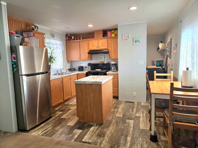 Kitchen with freestanding refrigerator, light countertops, dark wood finished floors, a center island, and ornamental molding
