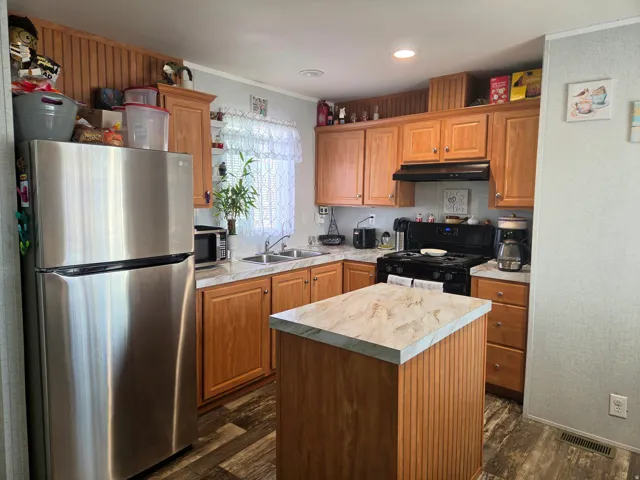 Kitchen featuring stainless steel appliances, light countertops, a kitchen island, dark wood finished floors, and ornamental molding