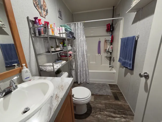 Bathroom with vanity, dark wood-style floors, shower / bath combo with shower curtain, and a textured wall