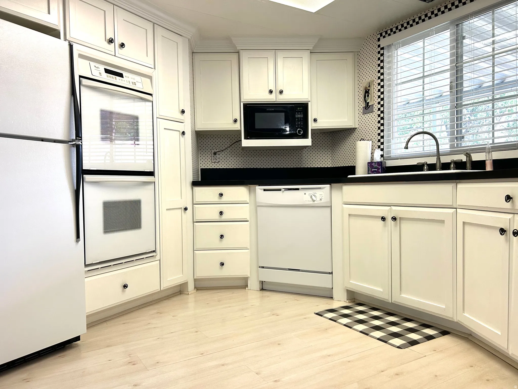 Kitchen featuring extensive white cabinetry with black hardware, black countertops, a built-in double oven, and wood-finish flooring
